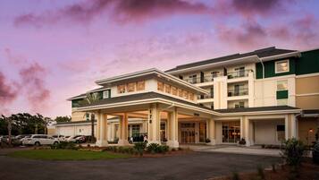 A multi-story hotel with a covered entrance, a parking lot, and a landscaped area with plants.