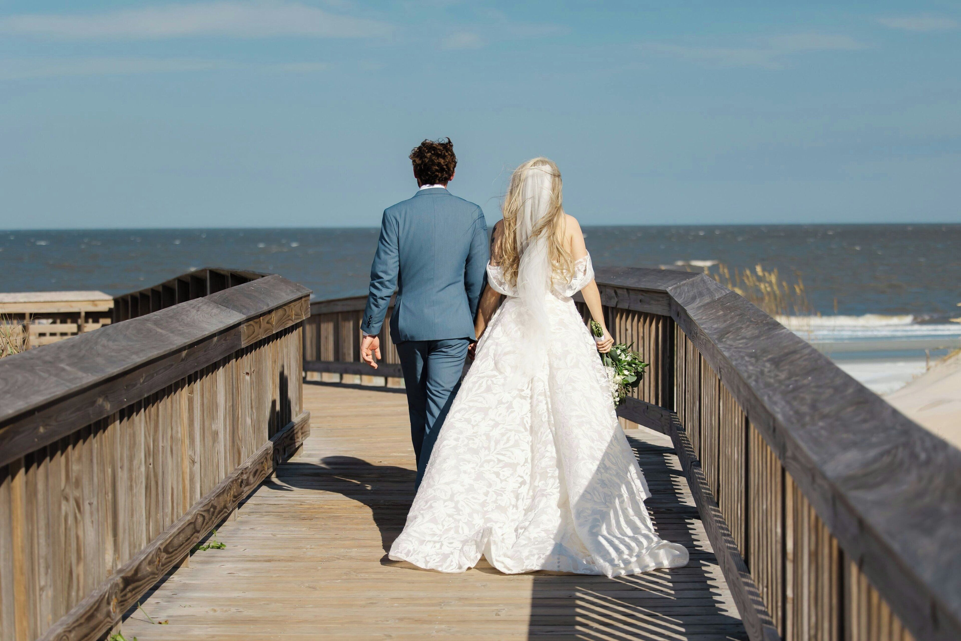 A wooden boardwalk leading to the beach with a couple walking.