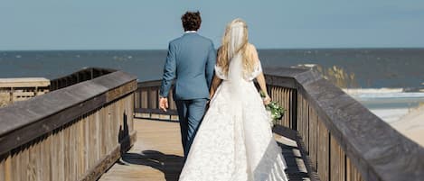 A wooden boardwalk leading to the beach with a couple walking.