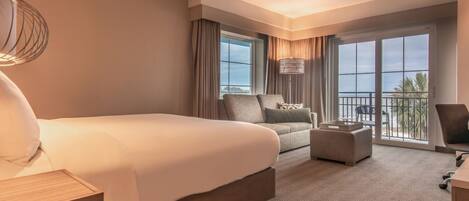 A hotel room with a large bed, a sofa, a desk, and a balcony with a view.