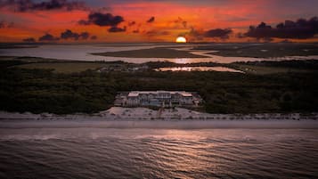 A coastal landscape with a sunset, a beach, and a large building with multiple stories.