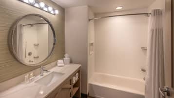 A modern bathroom with a large mirror, two sinks, a bathtub, and a shower.