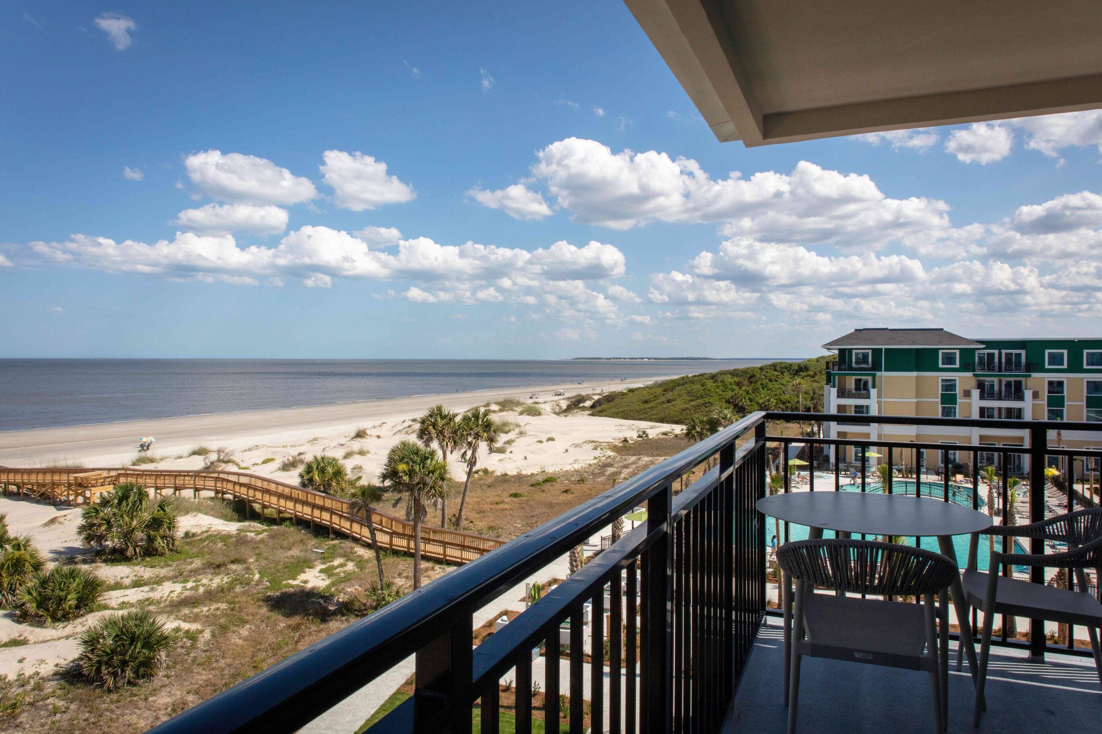 Un balcon avec vue sur la plage, un espace piscine et un immeuble à plusieurs étages.
