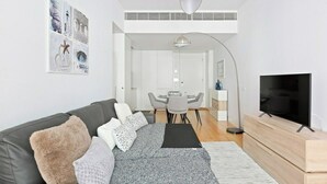 Ein modernes Wohnzimmer mit einer Couch, einem Fernseher und einem Essbereich mit Tisch und Stühlen.