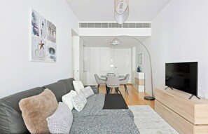 Ein modernes Wohnzimmer mit einer Couch, einem Fernseher und einem Essbereich mit Tisch und Stühlen.