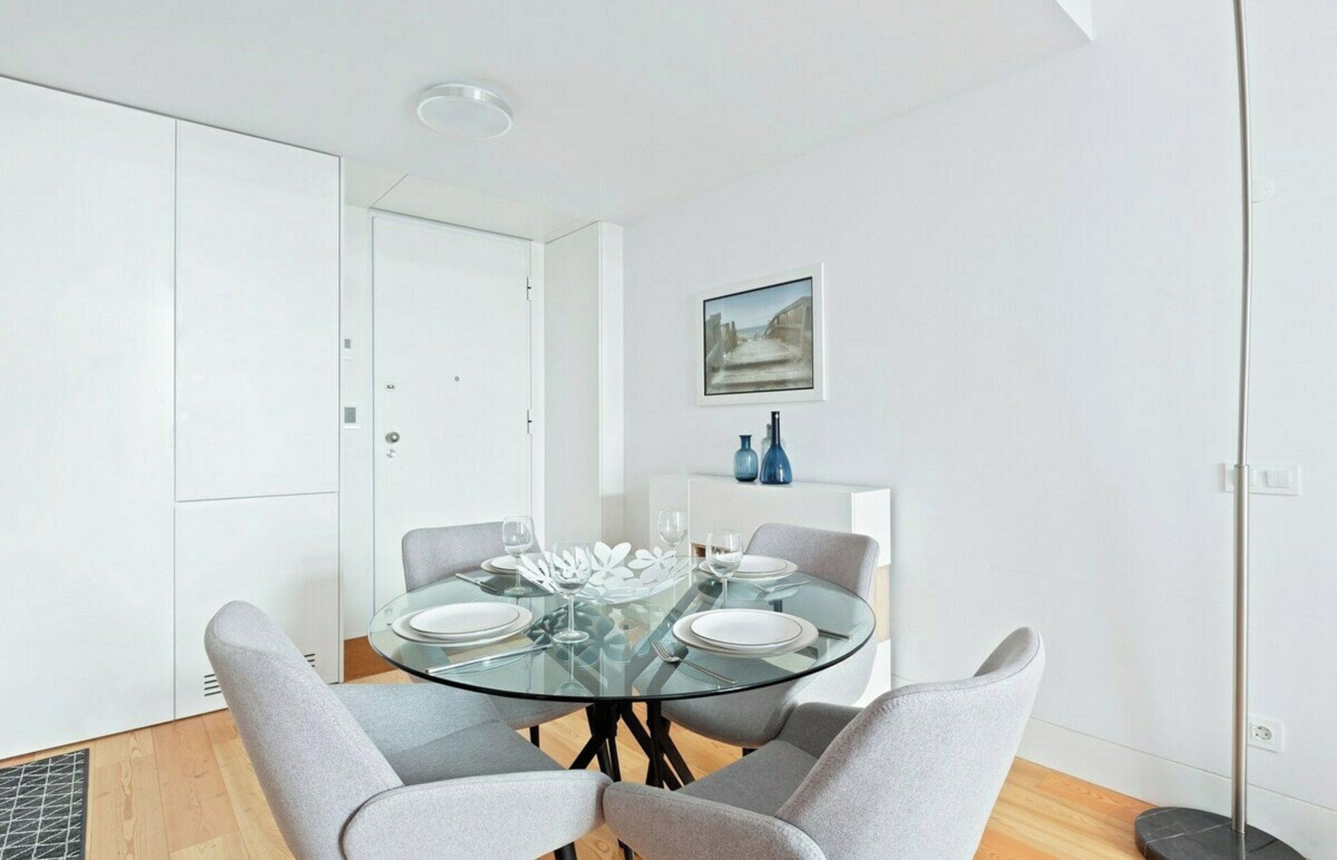 Un comedor moderno con una mesa de vidrio, sillas tapizadas grises y una puerta blanca al fondo.