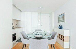 A modern dining area with a glass table, grey upholstered chairs, and a white cabinet with blue vases.
