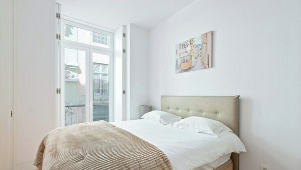Ein Schlafzimmer mit einem Bett, einem Nachttisch, einem Gemälde und Blick durch eine Glastür.