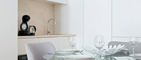 Una cocina moderna con cafetera integrada, un lavabo y un comedor con mesa de vidrio para cuatro.