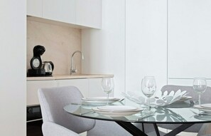 A modern kitchen with a built-in coffee maker, a sink, and a dining area with a glass table set for four.