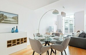 A modern dining area with a glass table, grey chairs, and a pendant light.