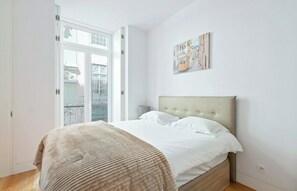 A bedroom with a bed, a nightstand, a painting, and a view through a glass door.