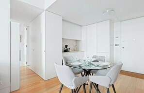 A modern dining area with a glass table, grey upholstered chairs, and white cabinetry. - Spacious 1 Bed Apartment near Baixa (Lisboa)