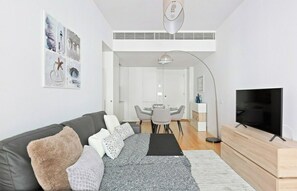 Uma sala de estar moderna com sofá, televisão e área de jantar com mesa e cadeiras.