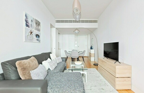 A modern living room with a sofa, a TV, and a dining area with a table and chairs.