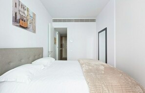 Quarto de hotel com cama, cabeceira, porta e quadro fixado na parede.