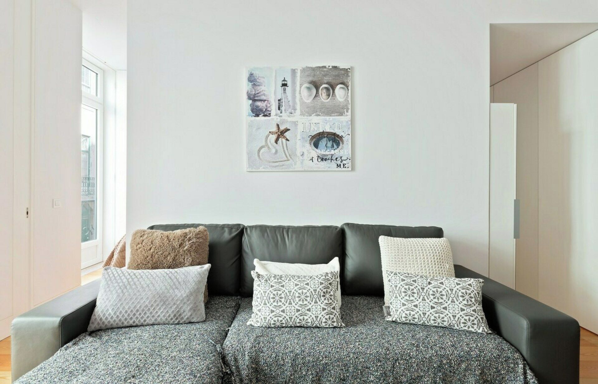 Ein Wohnzimmer mit einem schwarzen Ledersofa, drei gemusterten Kissen und einem Kunstwerk darüber.
