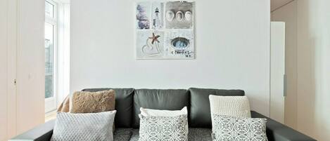 Ein Wohnzimmer mit einem schwarzen Ledersofa, drei gemusterten Kissen und einem Kunstwerk darüber.