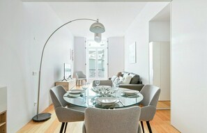 Ein moderner Essbereich mit einem Glastisch, grau gepolsterten Stühlen und einer Stehlampe.