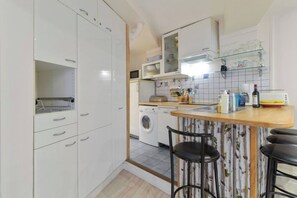 A compact kitchen with a washing machine, a microwave, and a bar area with stools.