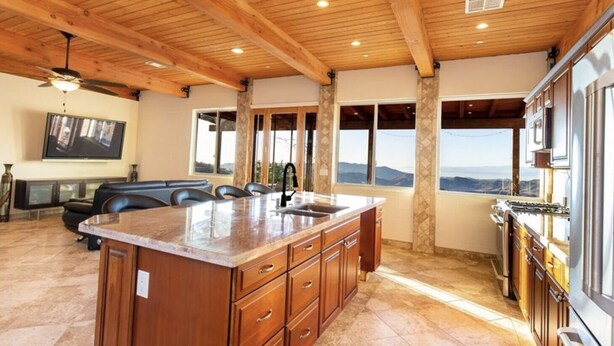 A spacious kitchen with a large island, wooden ceiling beams, and a view of the mountains. - Amazing Retreat with Unbelievable Views in Malibu (Malibu)