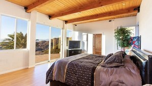 A bedroom with a large bed, a TV, and a sliding glass door leading to a balcony with a view of the desert. - Amazing Retreat with Unbelievable Views in Malibu (Malibu)