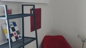 Ein Zimmer mit einem schwarzen Metallregal, einem roten Sessel, einem kleinen gelben Beistelltisch und einem Bild an der Wand.