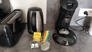 Eine Küchenarbeitsplatte mit einem Toaster, einer Kaffeemaschine und zwei kleinen Gläsern mit Portionsbeuteln.