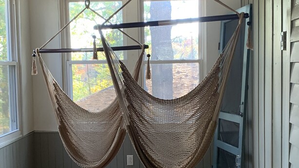 A room with two hammocks suspended from the ceiling, a wooden floor, a potted plant, and a view of the outdoors through large windows.