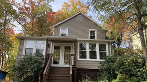A two-story house with a front porch, a staircase leading to the entrance, and a garden area with various plants and trees.