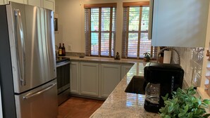 A kitchen with white cabinets, a stainless steel refrigerator, a coffee maker, and a window with blinds.