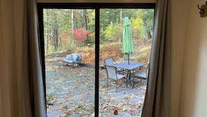 A sliding glass door leading to an outdoor patio with a table and chairs, surrounded by autumn foliage.