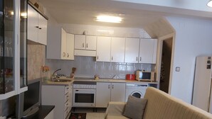 Una cocina compacta con armarios blancos, microondas, lavadora y sofá.