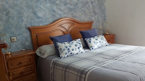 Un dormitorio con cabecera de madera, dos mesitas de noche con lámparas, cama con colcha a cuadros y una pared con textura.