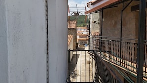 Un balcón estrecho con suelo de baldosas y barandilla de metal.