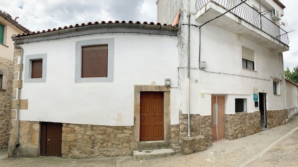 Un edificio de dos pisos con fachada blanca, base de piedra y puerta marrón.