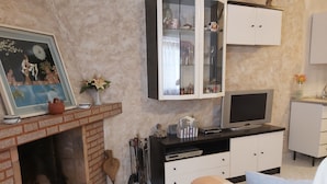 Una sala de estar con chimenea, televisor, aparador con puertas de vidrio y una cama con manta a cuadros.