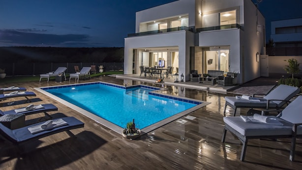 Ein modernes, zweistöckiges Haus mit Schwimmbad, Außenbereich mit Sitzgelegenheiten und einer gut beleuchteten Terrasse.