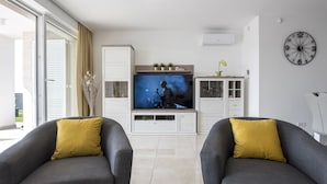 Ein Wohnzimmer mit zwei grauen Sesseln, einem Fernseher, einer weißen Kommode und einer Wanduhr.