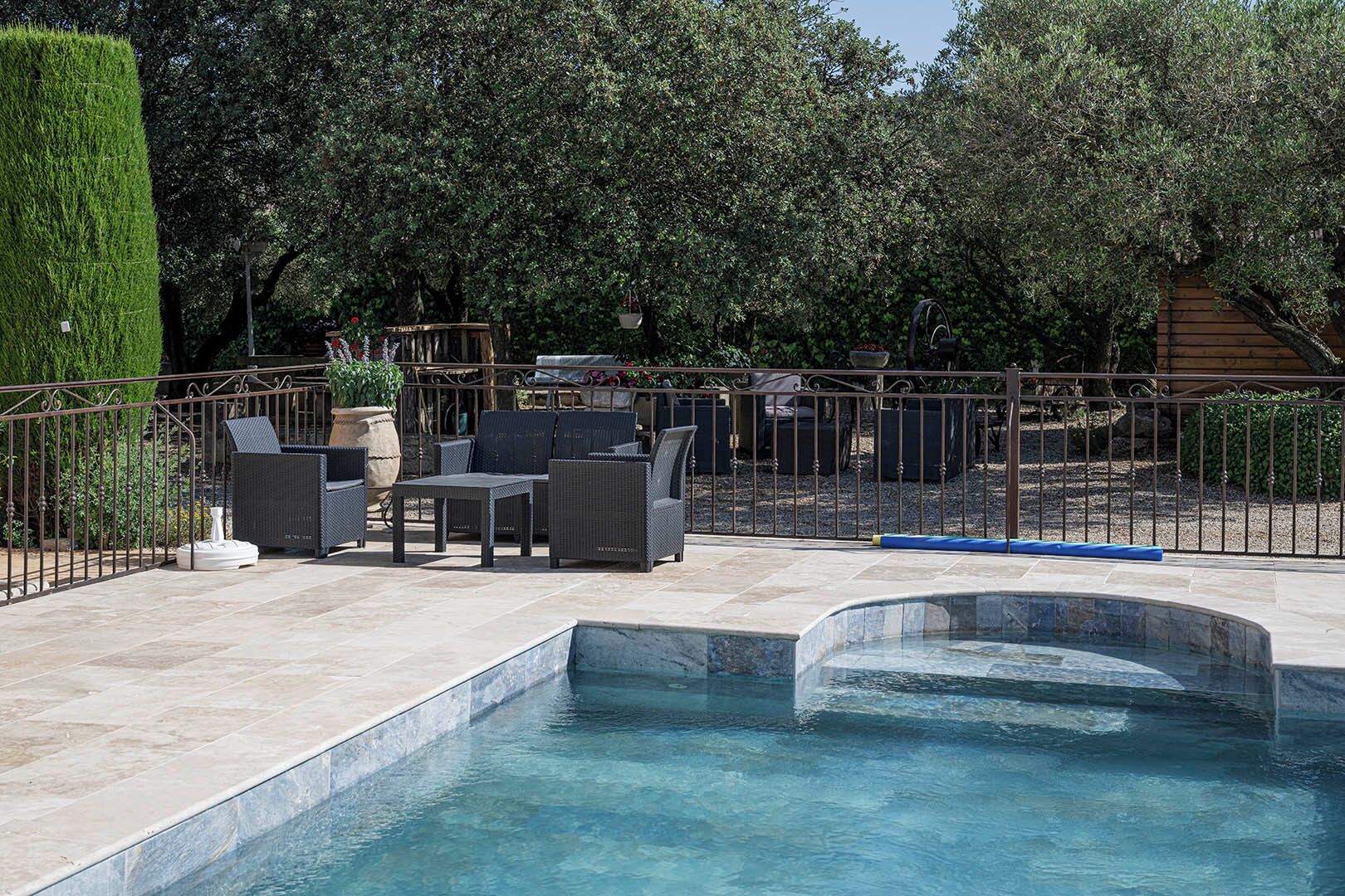 A swimming pool with a tiled deck, surrounded by a metal fence, and outdoor furniture.