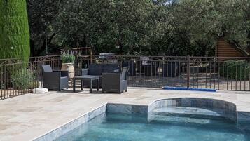 A swimming pool with a tiled deck, surrounded by a metal fence, and outdoor furniture.