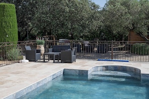A swimming pool with a tiled deck, surrounded by a metal fence, and outdoor furniture. - Chambre d'hôtes les cigales (Comps)
