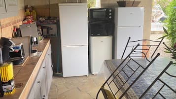 A kitchen with a dining area, featuring a stone floor, a dining table with metal chairs, a hanging light fixture, and a wall-mounted clock.