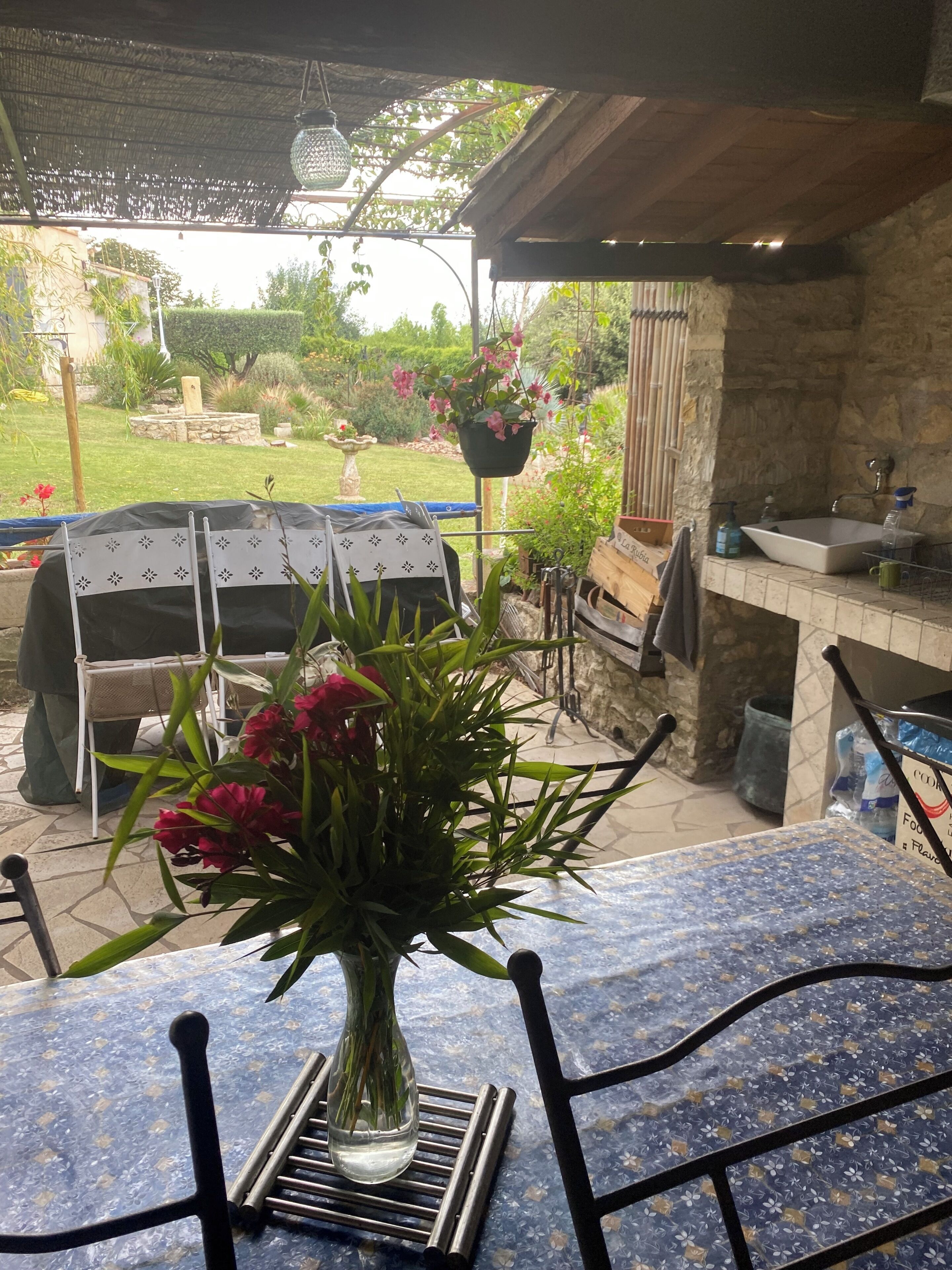 Une terrasse extérieure avec une table, des chaises, un barbecue et un pot de fleurs suspendu.