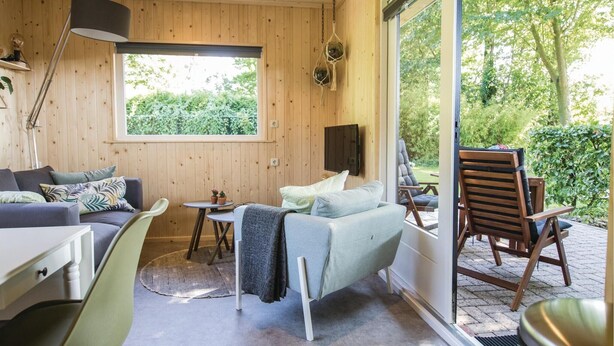 Een gezellige kamer met een bank, een eettafel en een stoel. Er is een raam met uitzicht op groen.