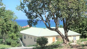 A single-story building with a sloped roof, a staircase leading to the entrance, and a view of the ocean in the background.