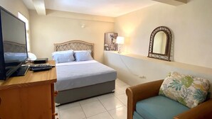 A hotel room with a bed, a desk with a television, a chair, and a mirror on the wall.