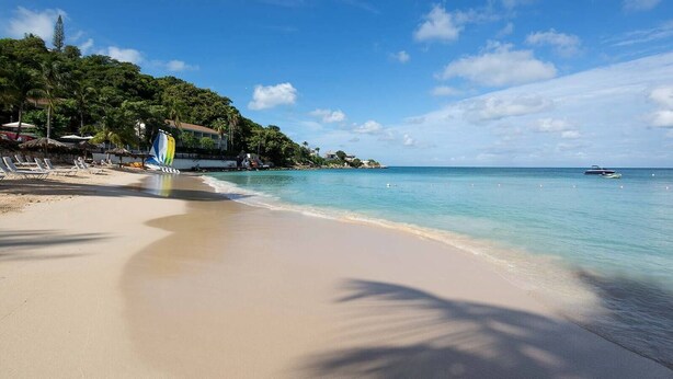 A beach with clear water, lounge chairs, and a sailboat.