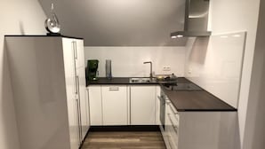 Moderni keittiö, jossa on valkoiset kaapit, musta työtaso ja puulattia.