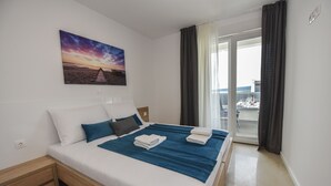 Cama bem arrumada com roupa de cama azul e branca, mesa de cabeceira de madeira e um quadro com pôr do sol na parede.